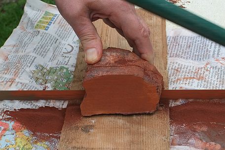 Het afzagen van een plak rood natuurkrijt van een brok r&ouml;tel