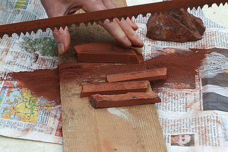 Het zagen van stiften uit een plak r&ouml;tel (rood natuurkrijt)